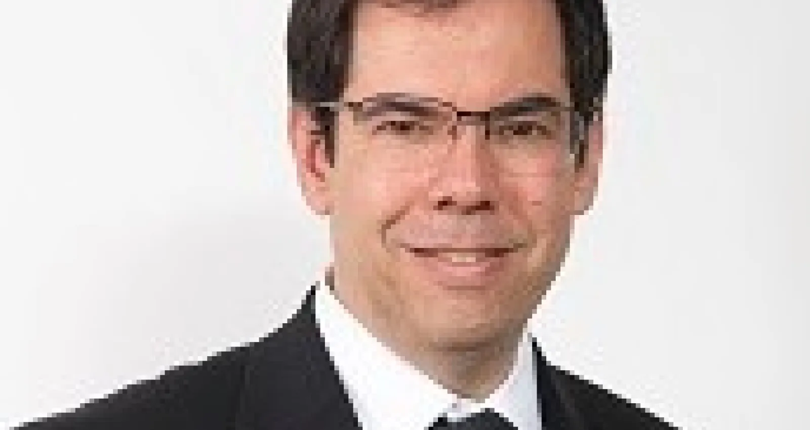Hombre con traje y gafas cuadradas sonriendo a la cámara 