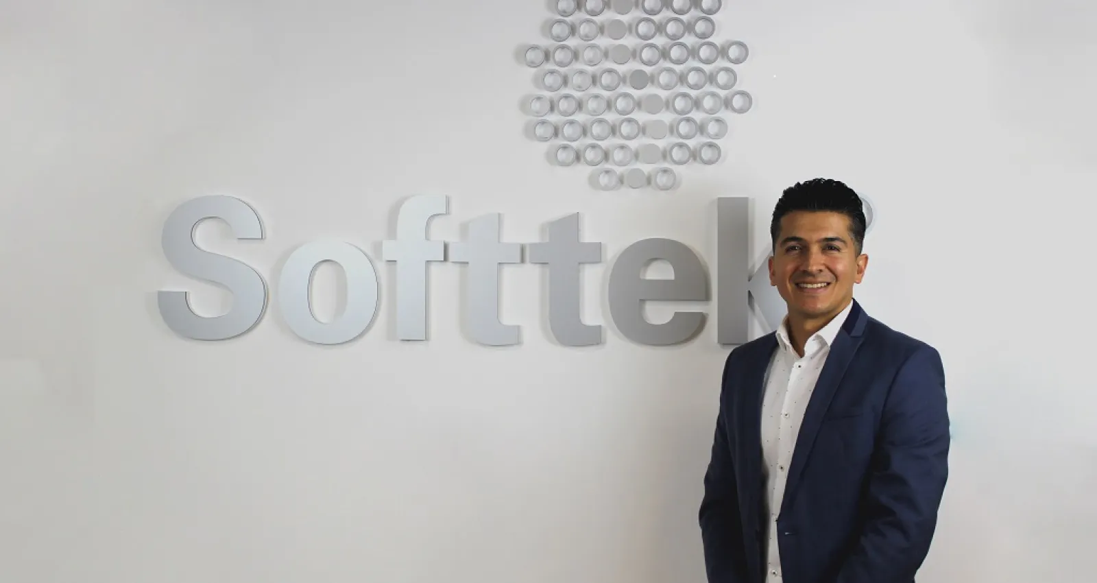Foto de una persona con traje frente a un letrero de softtek