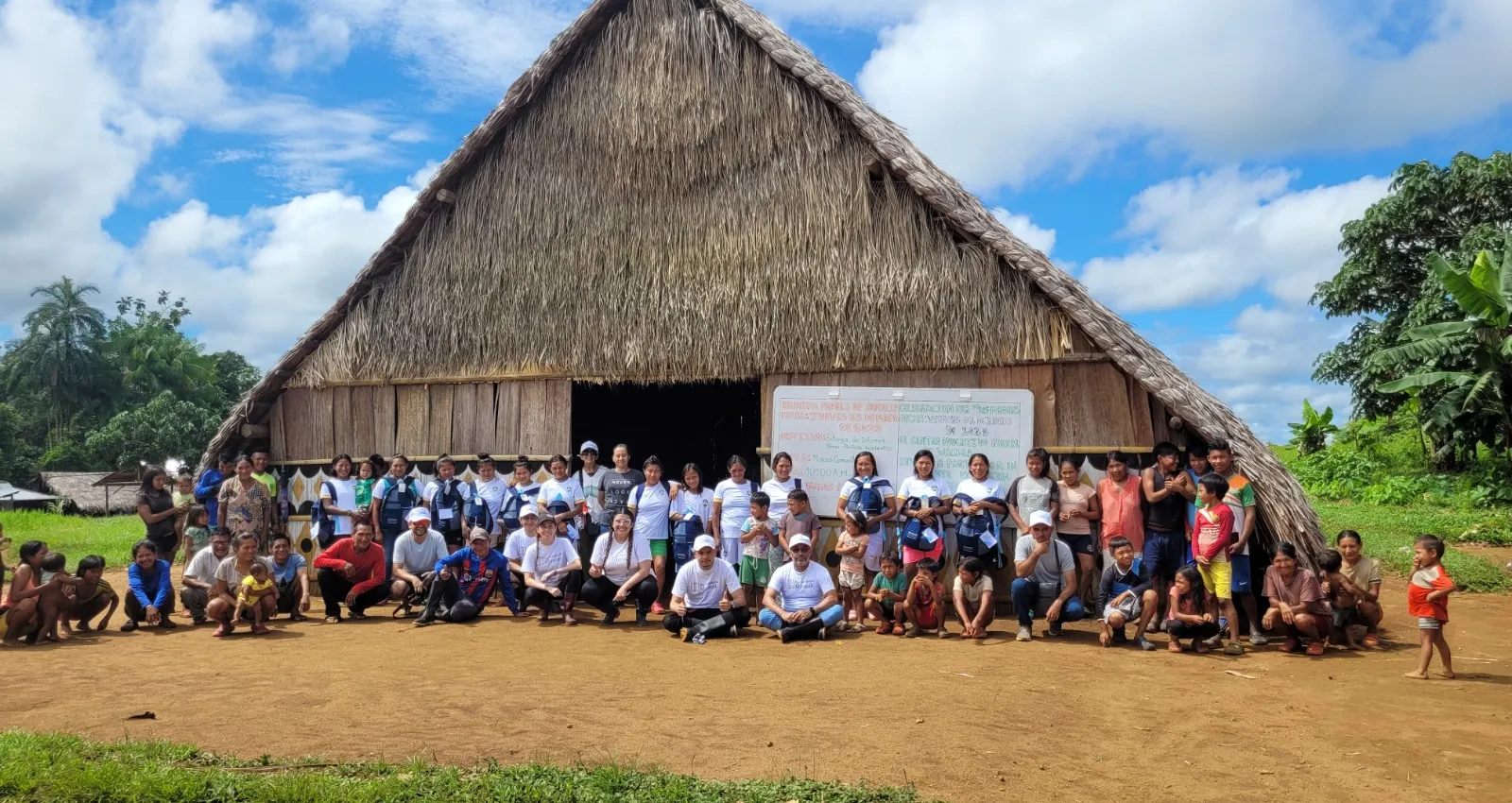 Foto de una casa en paja con 30 personas al frente de ella posando para una fotografía
