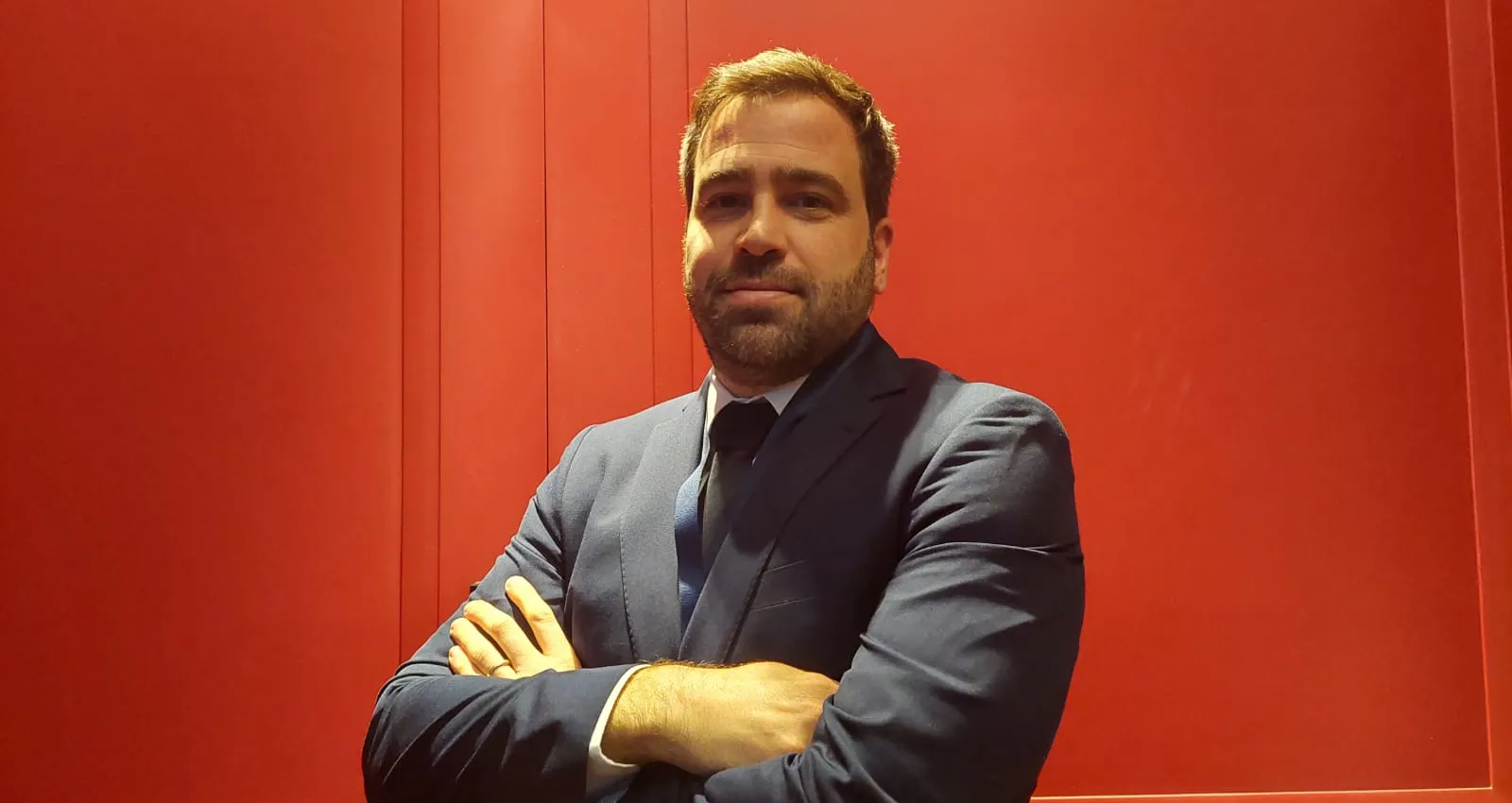 Hombre blanco y con barba cruzando sus brazos y mirando hacía la cámara