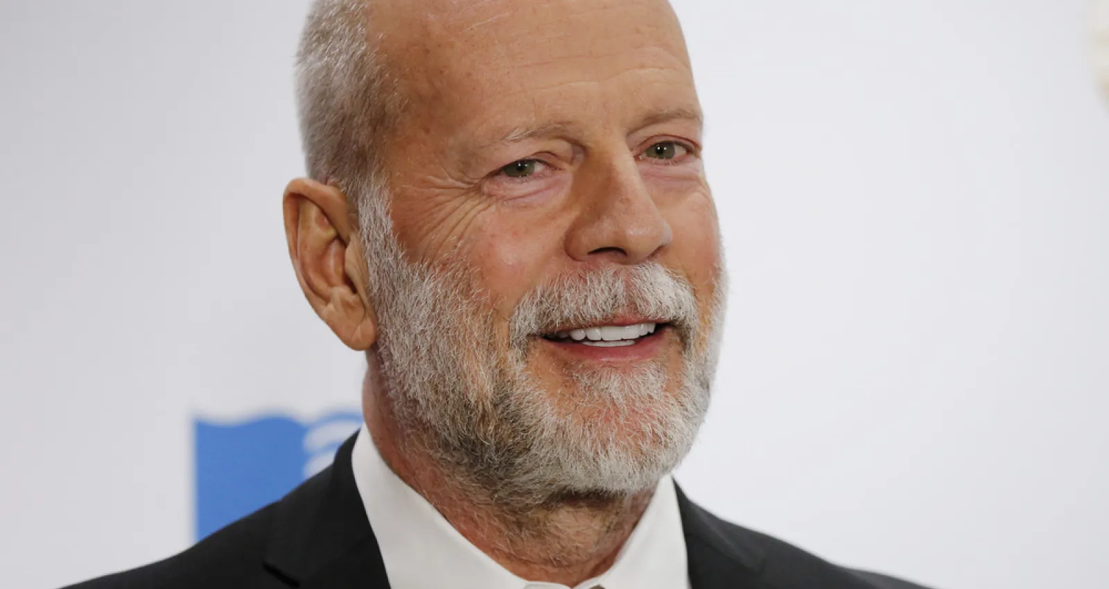 Foto de bruce willis, un señor con barba en traje y fondo blanco