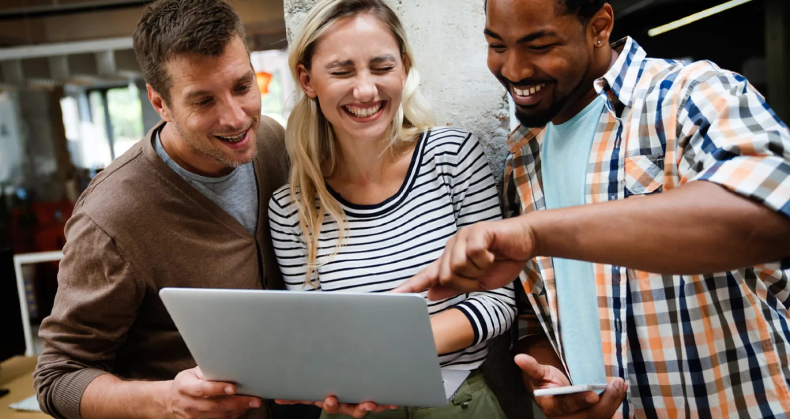 Foto de tres personas mirando un computador y sonriendo a la cámara