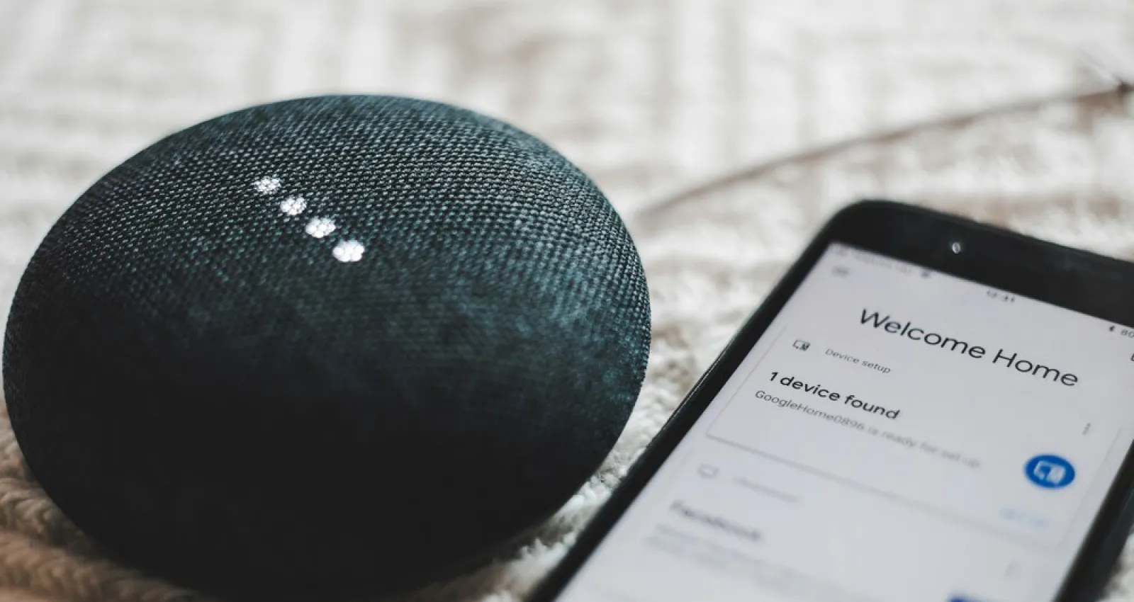 Foto de un celular y una alexa al costado, dispositivo electrónico