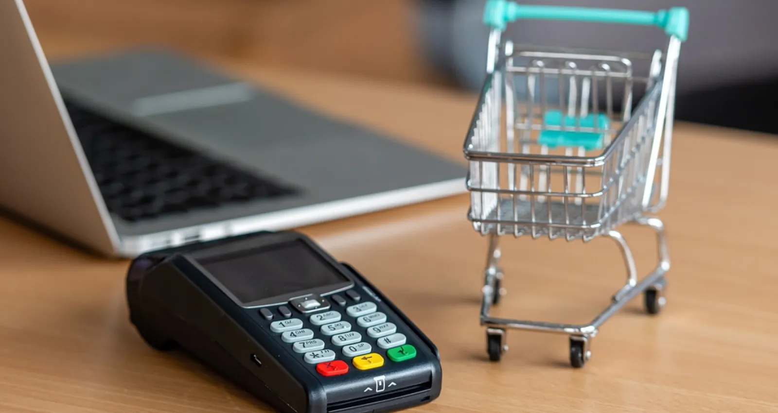 Foto de un datafono con un computador al fondo y al costado un carrito de compras