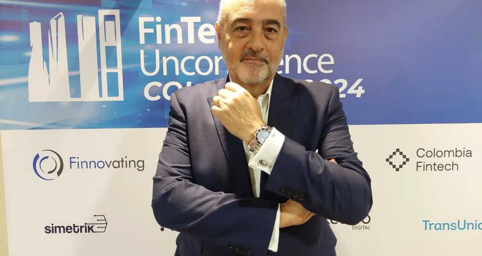 Foto de un ejecutivo mirando a la cámara con la mano en el mentón y un fondo comercial del evento
