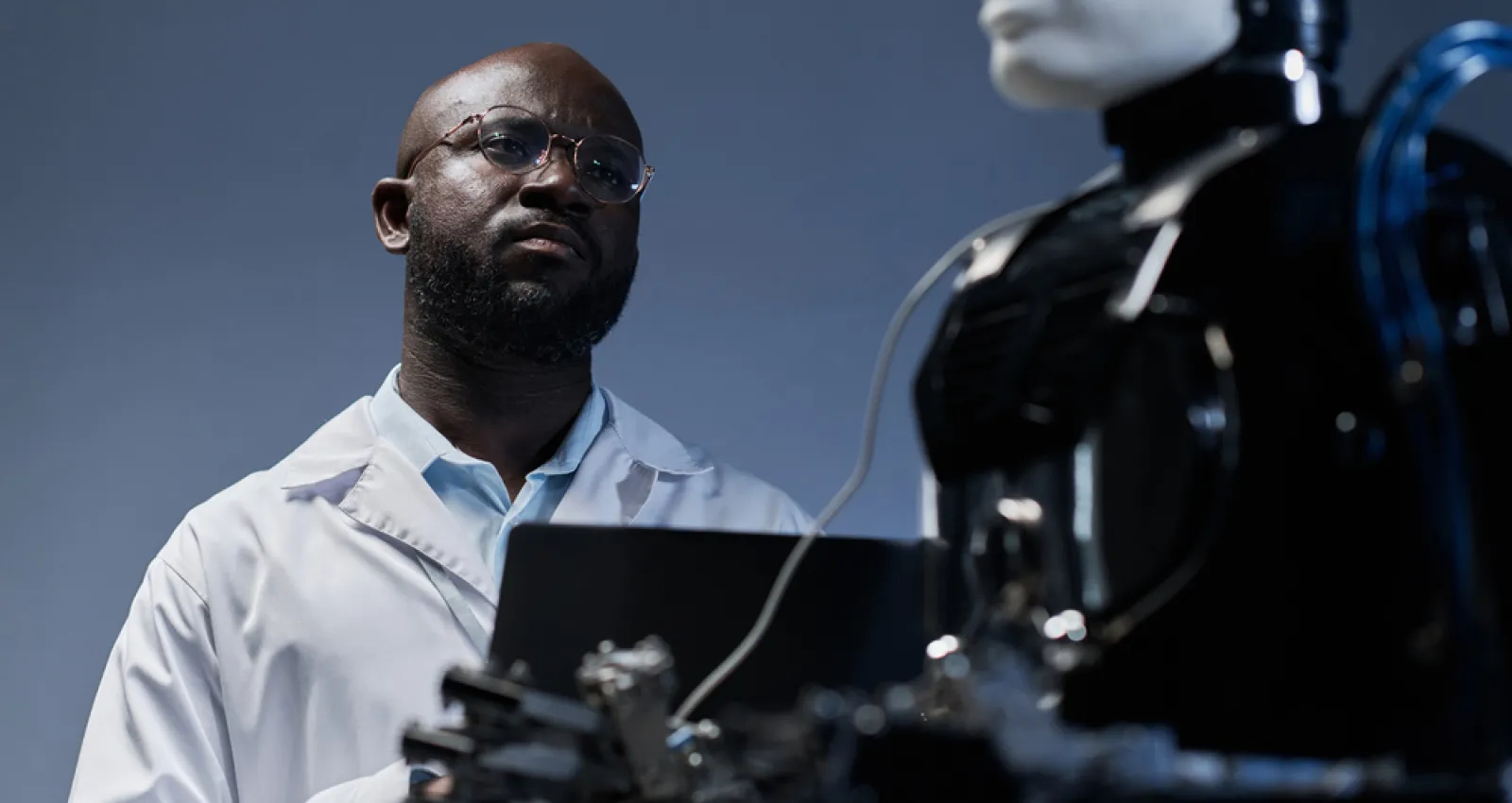 Foto de un hombre americano escribiendo sobre un teclado y mirando un robot