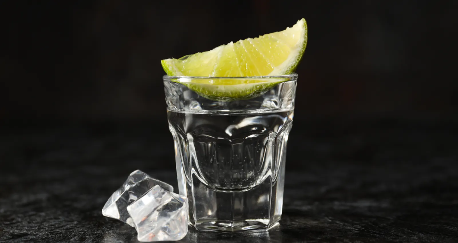 Foto de una copa para tomar licor con un limón encima y un fondo negro