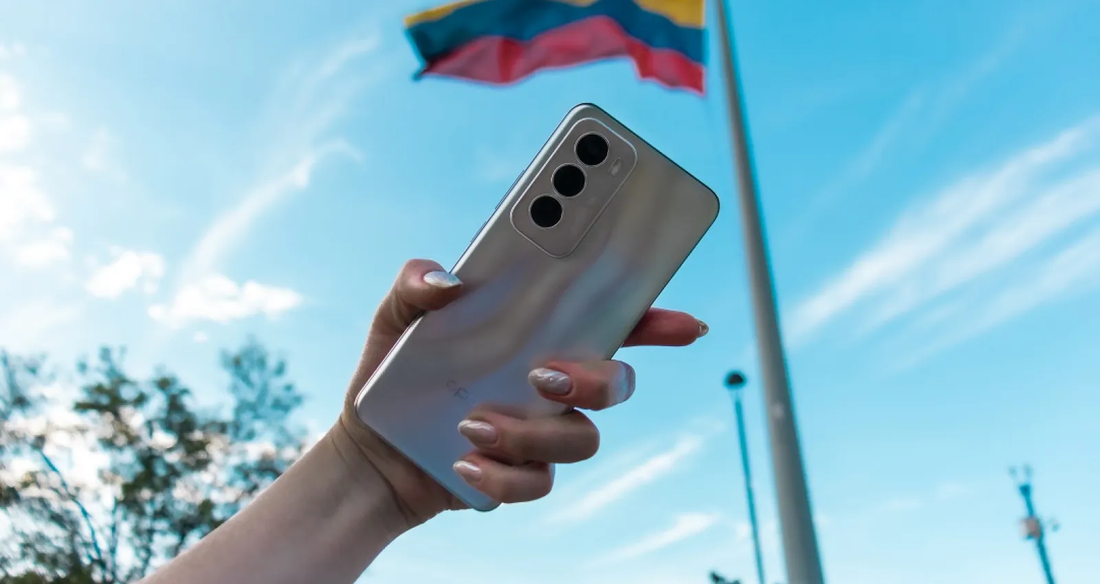 Foto de una mano de mujer con un celular y una bandera de fondo