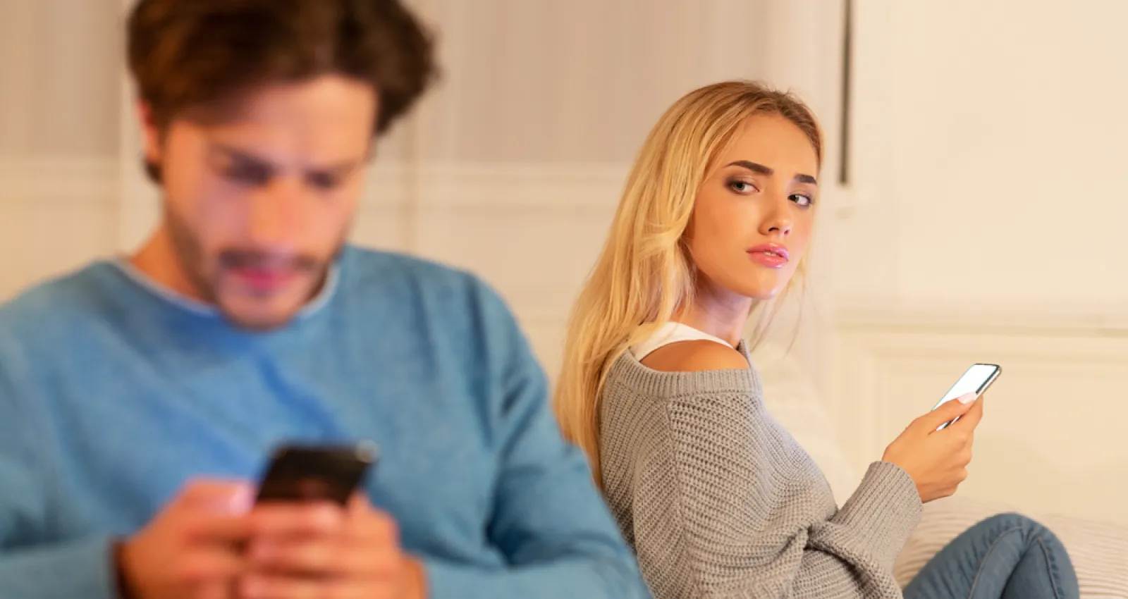 Foto de una mujer con un celular en la mano mirando de forma sospechosa a su pareja que habla por celular