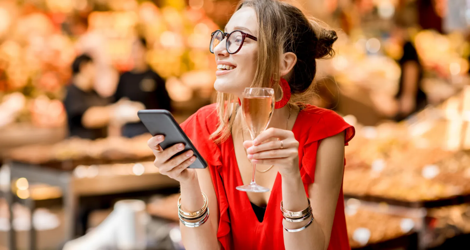 Foto de una mujer con un celular en la mano y una copa en la otra