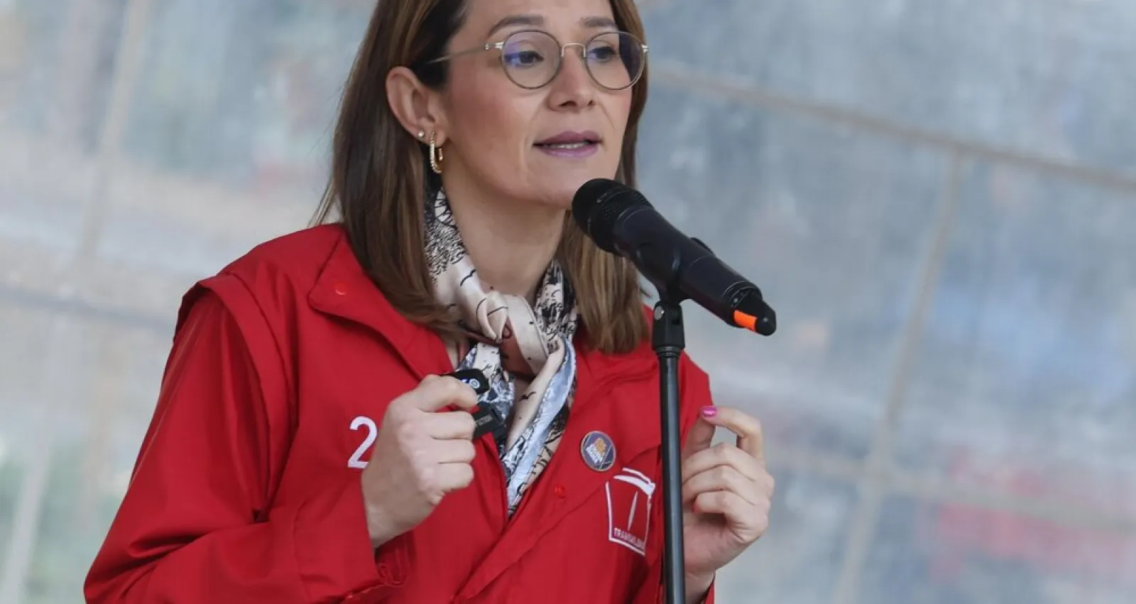 Foto de una mujer hablandole a un microfono con una chaqueta roja