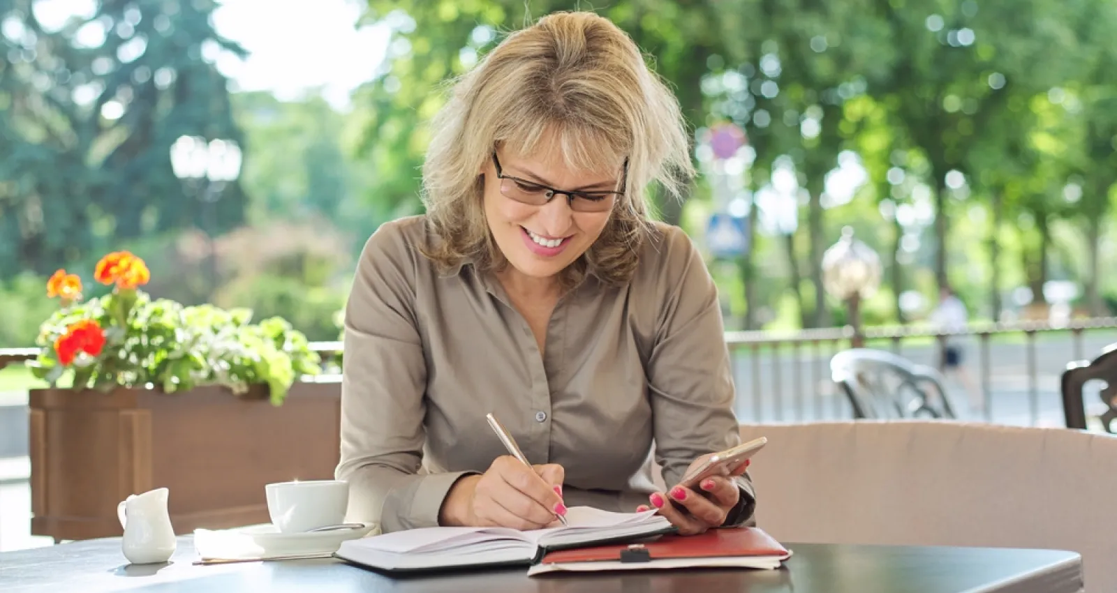 Foto de una mujer rubia anotando algo en un cuaderno con un fondo de arboles