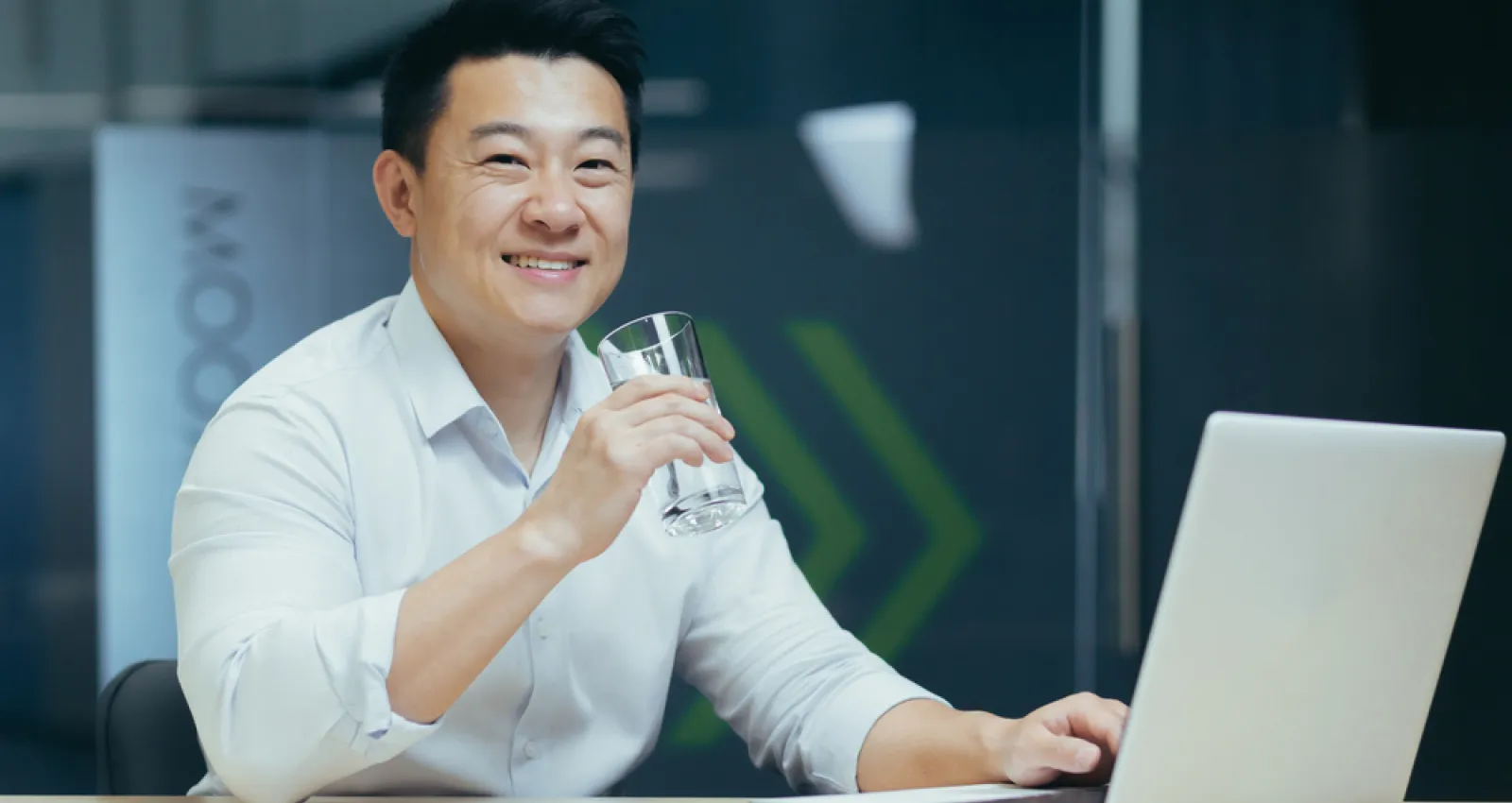 Foto de una persona asiática tomando agua con un computador en su mano