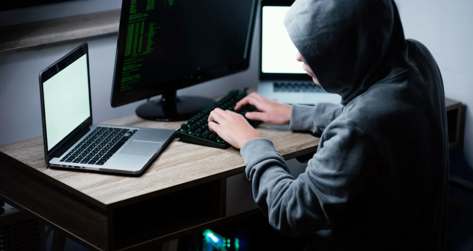 Foto de una persona con una capucha trabajando con un computador 