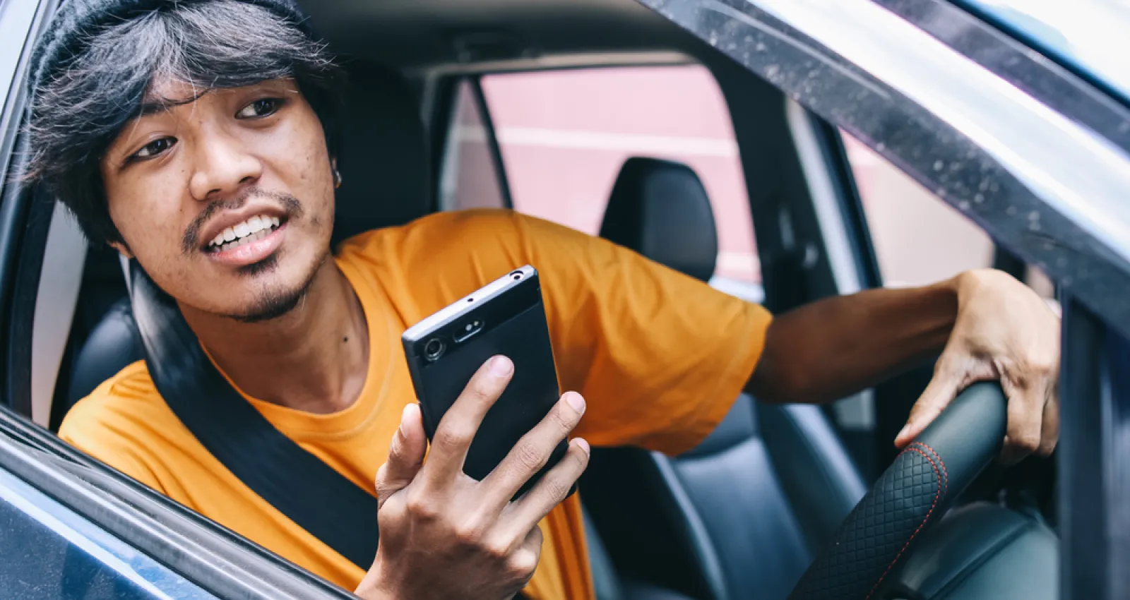Foto de una persona sacando la cabeza por la ventana con un celular en la mano