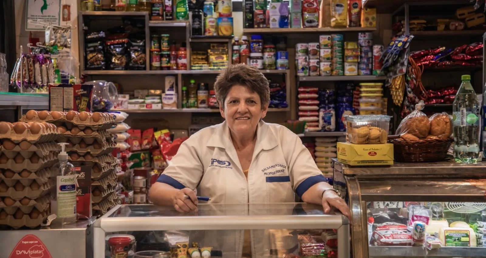 Foto de una señora frente a unos stands de una tienda de barrio