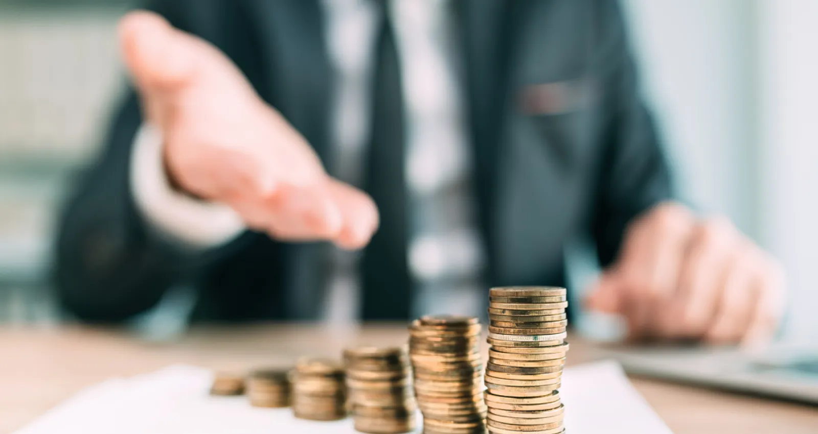 Foto de unas monedas apiladas y de fondo un señor de traje