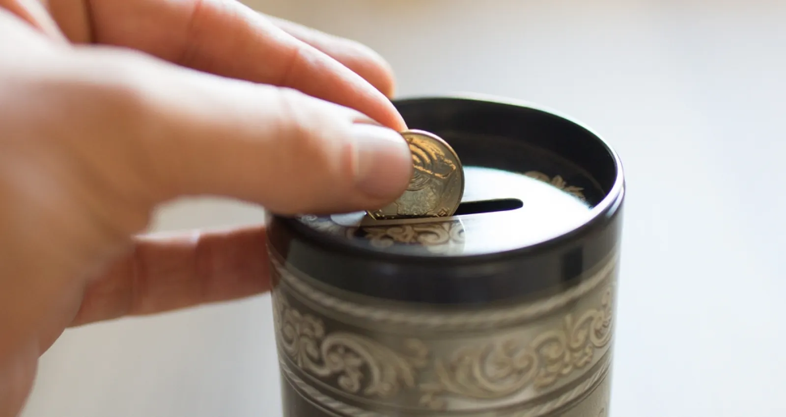 Foto de unos dedos ingresando unas monedas en la alcancia
