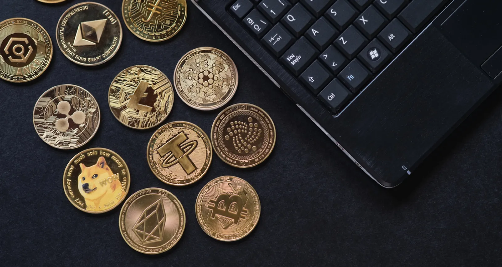 Foto de varias monedas cripto sobre una mesa con un computador al costado derecho