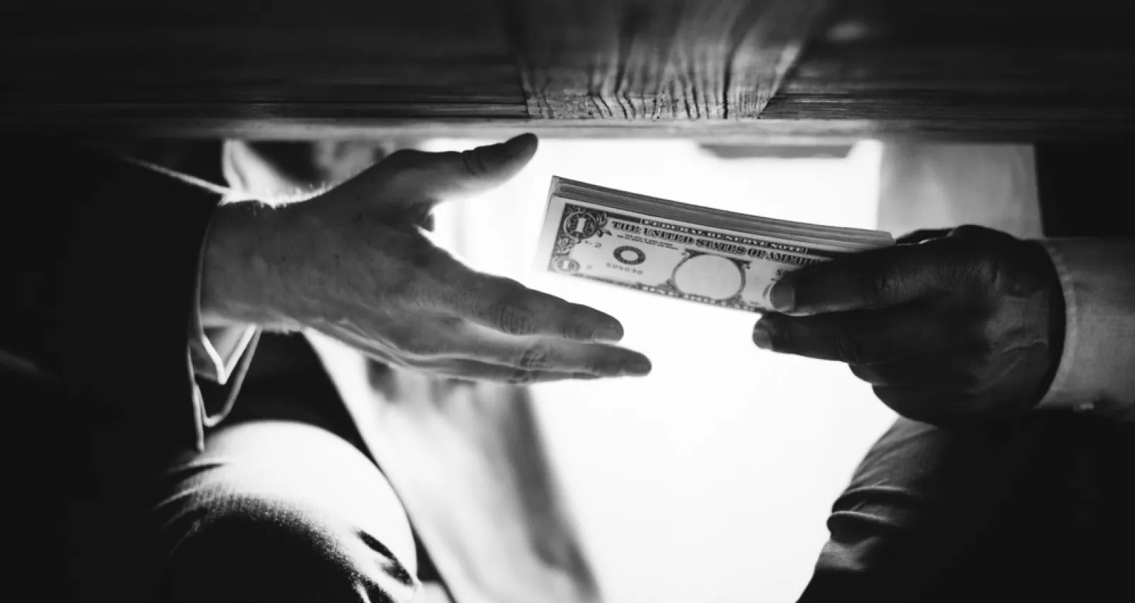 Foto de dos personas pasando dinero por debajo de la mesa