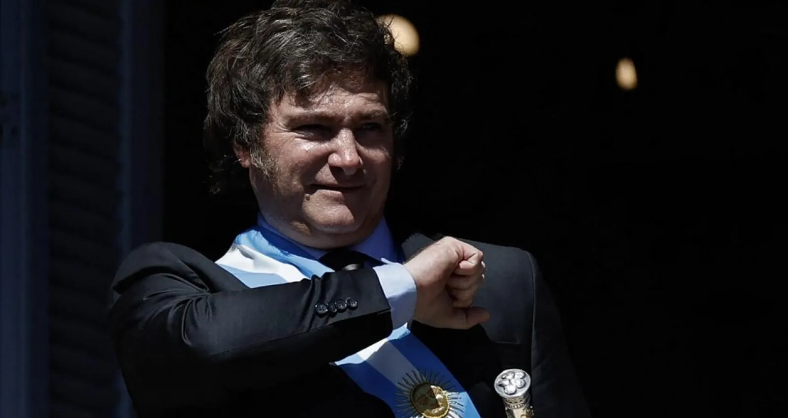 Fotografia de una persona con pelo en la frente y traje con una bandera de argentina en su costado
