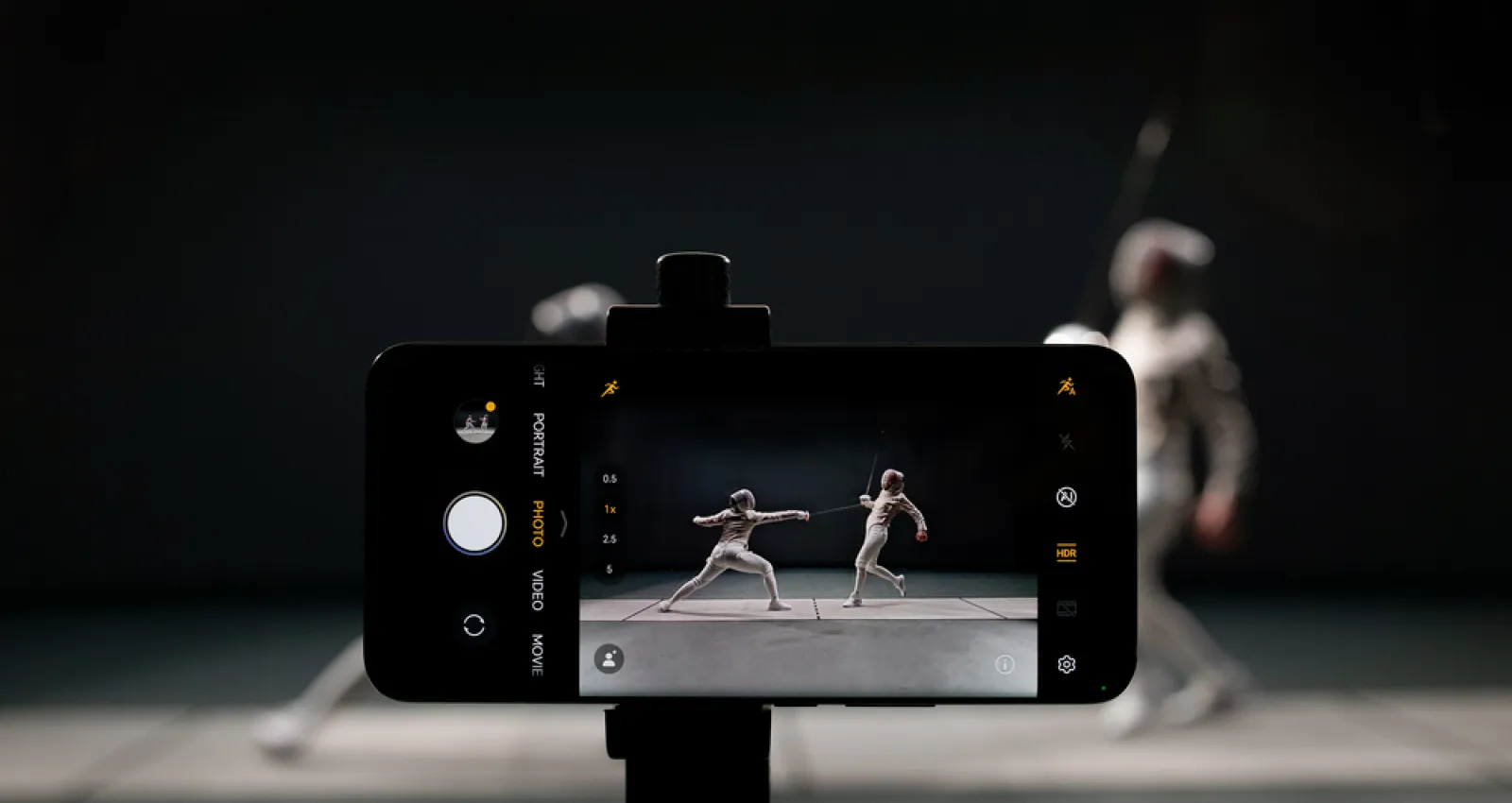 Foto de una celular tomando una foto de dos personas jugando esgrima con fondo negro