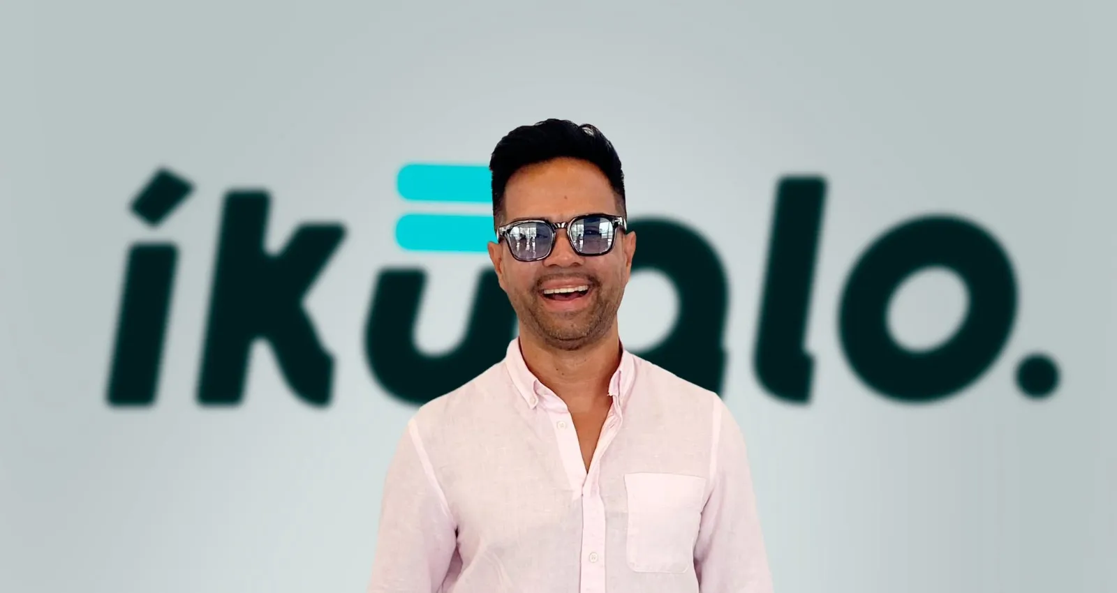 Fotografía de un hombre sonriendo con unas gafas y de fondo el nombre de Ikualo