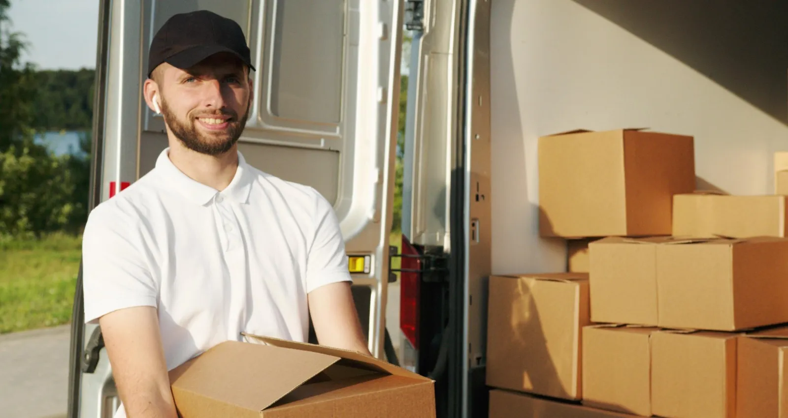Foto de un un hombre con camiseta blanca y gorra negra alzando una caja sonriendo a la cámara