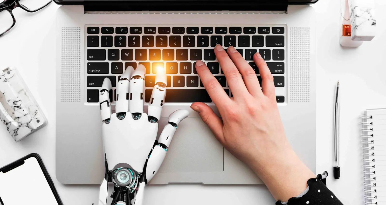 Foto de una mano biónica y humana escribiendo sobre un pc