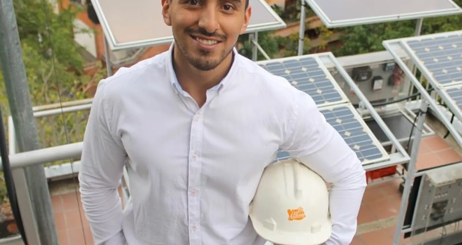 Foto de una persona con un casco posando frente a la cámara con unos paneles solares de fondo