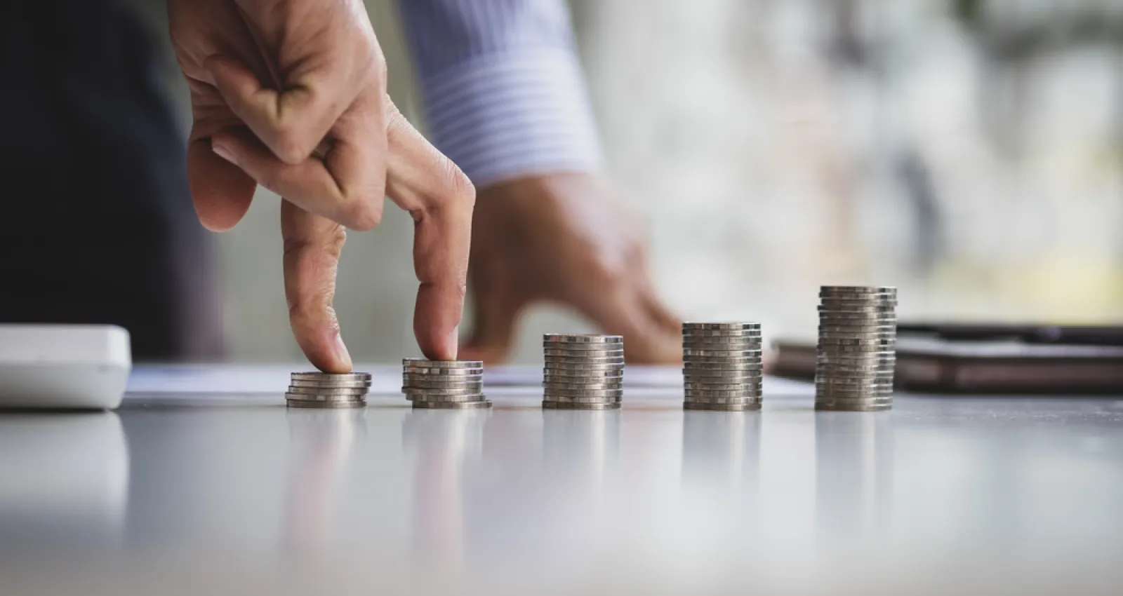 Monedas en una mesa y unos dedos pasando por ellas de forma escalonada