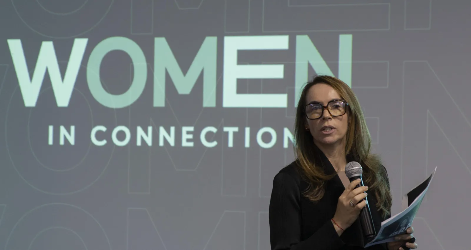 Mujer hablando en un escenario profesional con un fondo que dice Women
