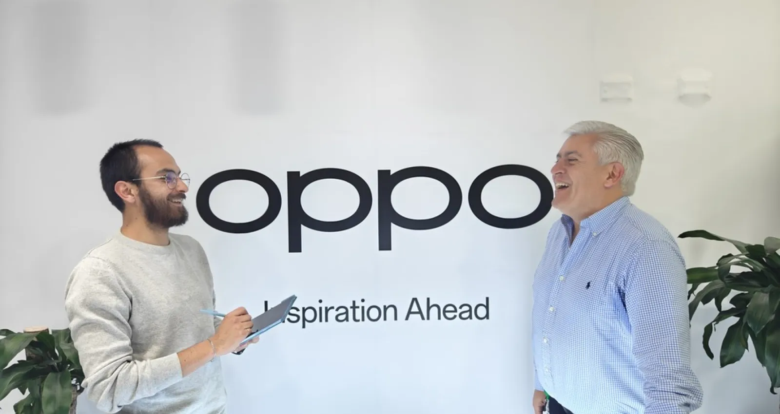 Fotografía de dos personas hablando con un letrero de fondo que dice Oppo