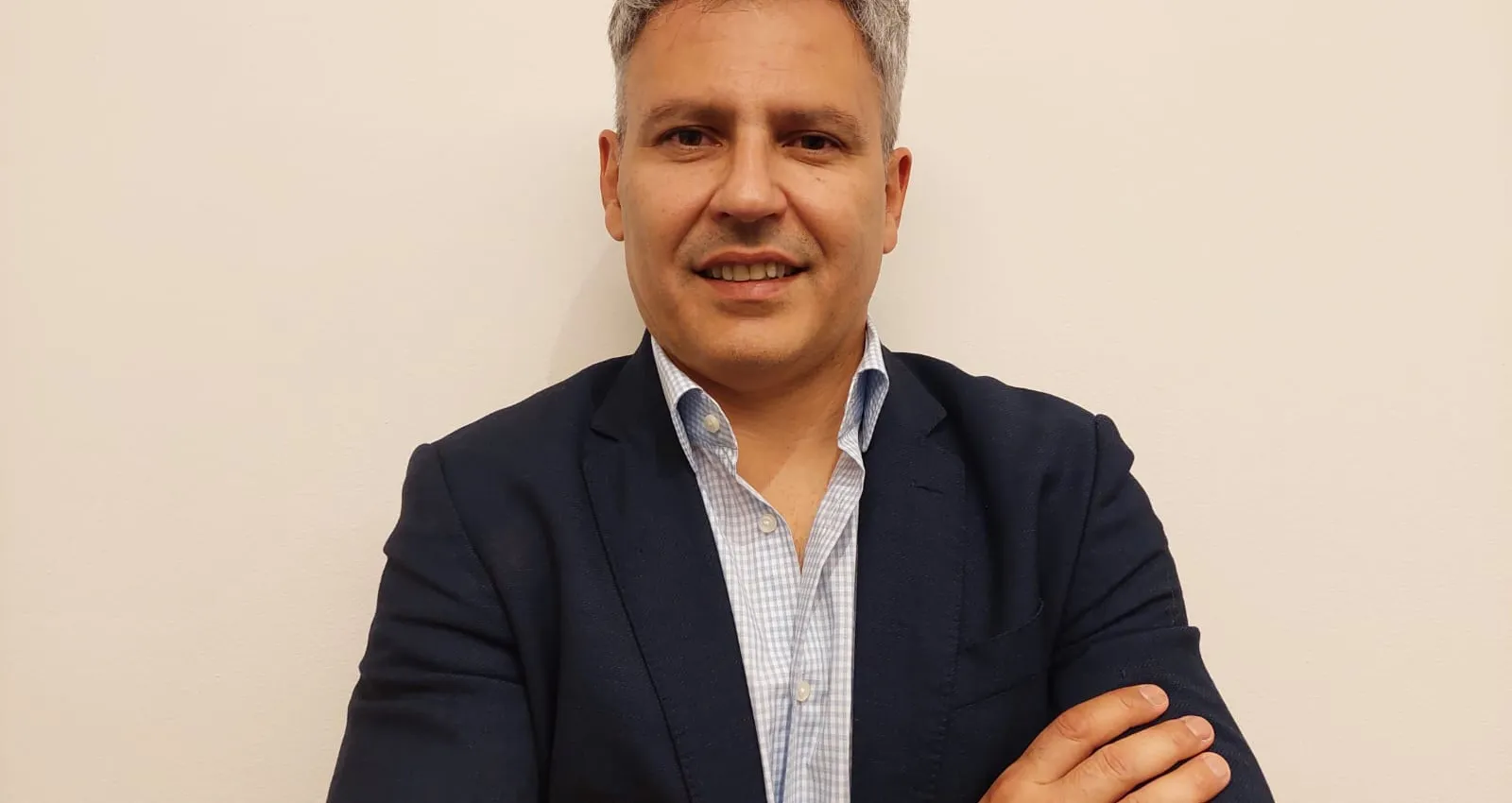 Foto de una persona posando frente a la cámara, cuenta con camiseta, blazer negro, reloj y pelo blanco