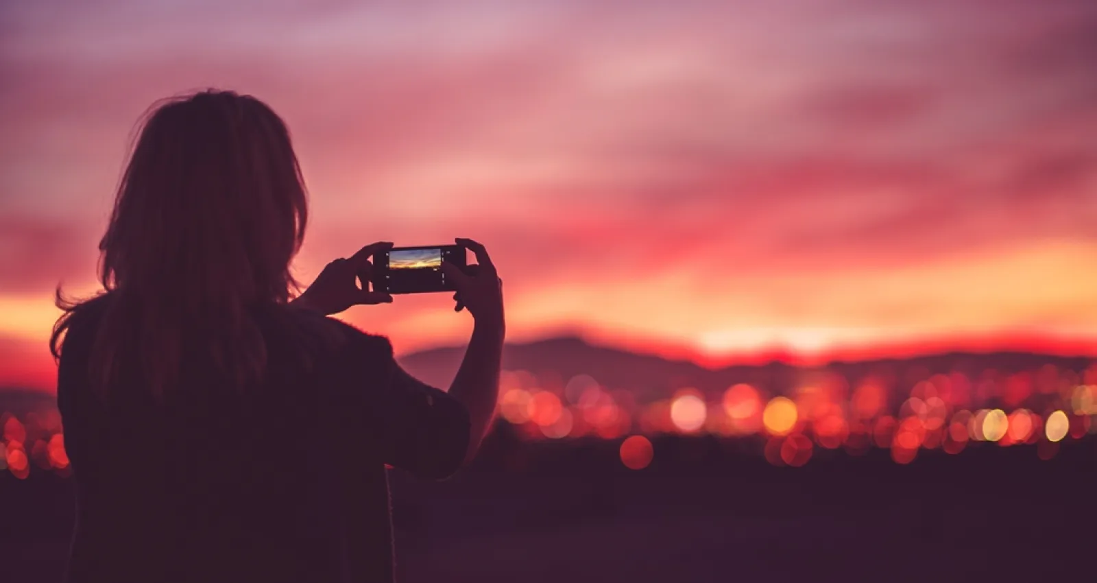 Una mujer tomando una foto sobre un cielo rosado y naranja