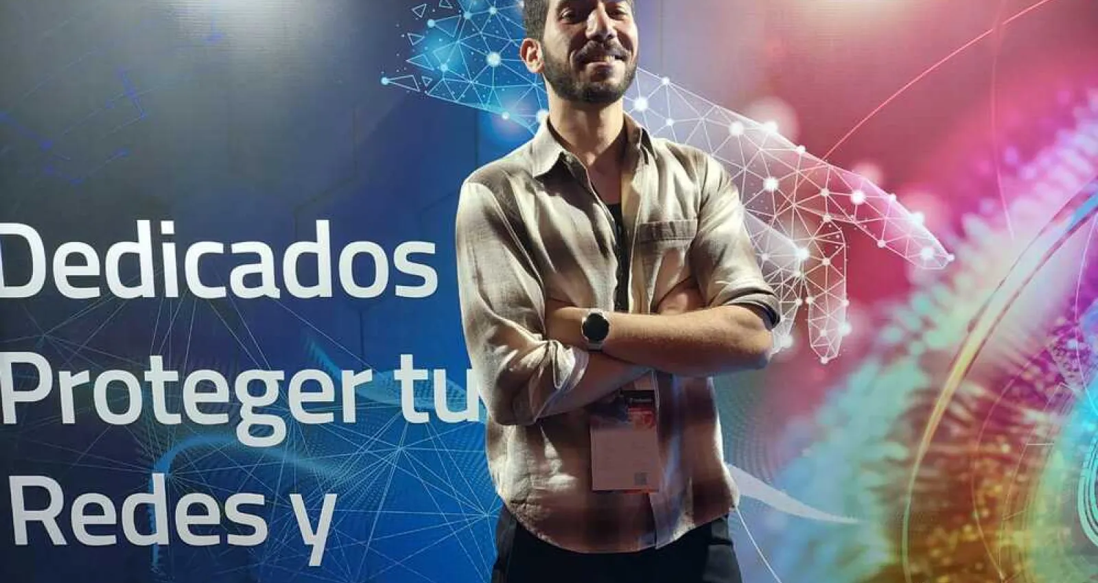 Foto de una persona cruzada de brazos con un fondo que dice dedicados a proteger tus redes y aplicaciones