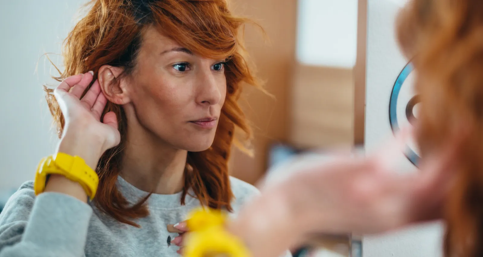 Una mujer tocandose la oreja frente al espejo