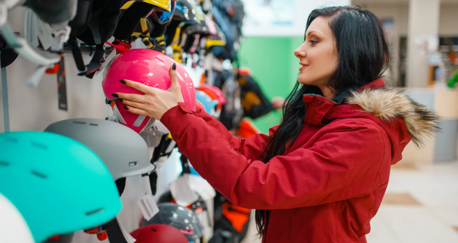 Una mujer con chaqueta roja toma un casco  rosado de un local 