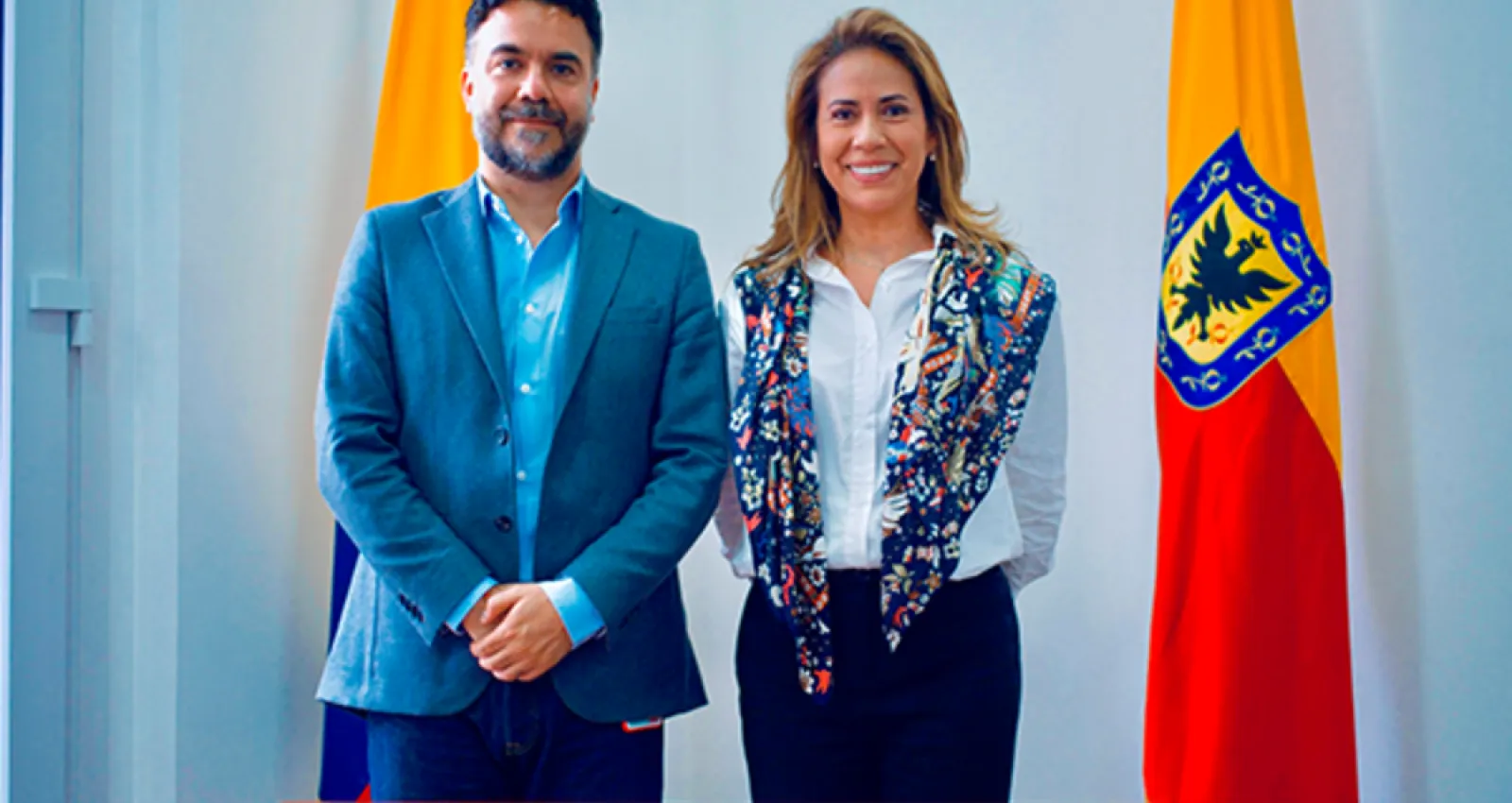 foto de un hombre y una mjer posando frente a la cámara con la bandera de bogotá al costado derecho