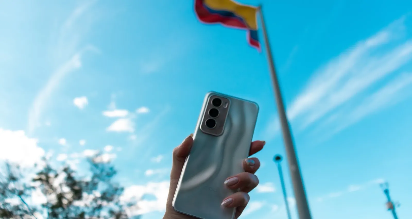 foto de una mano sosteniendo un celular con una bandera de fondo