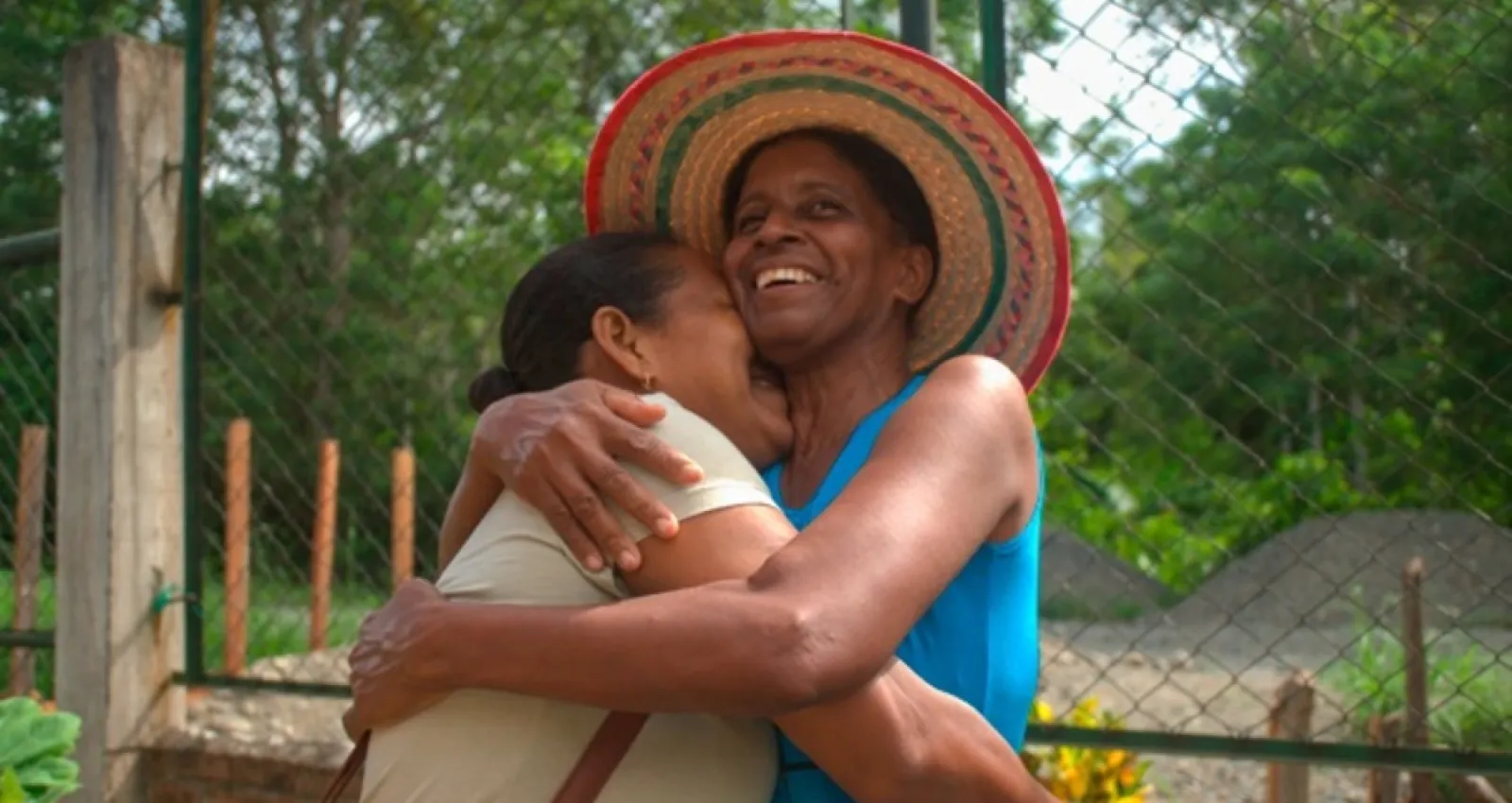 Mujeres abrazandose, una de ellas tiene un sombrero colorido