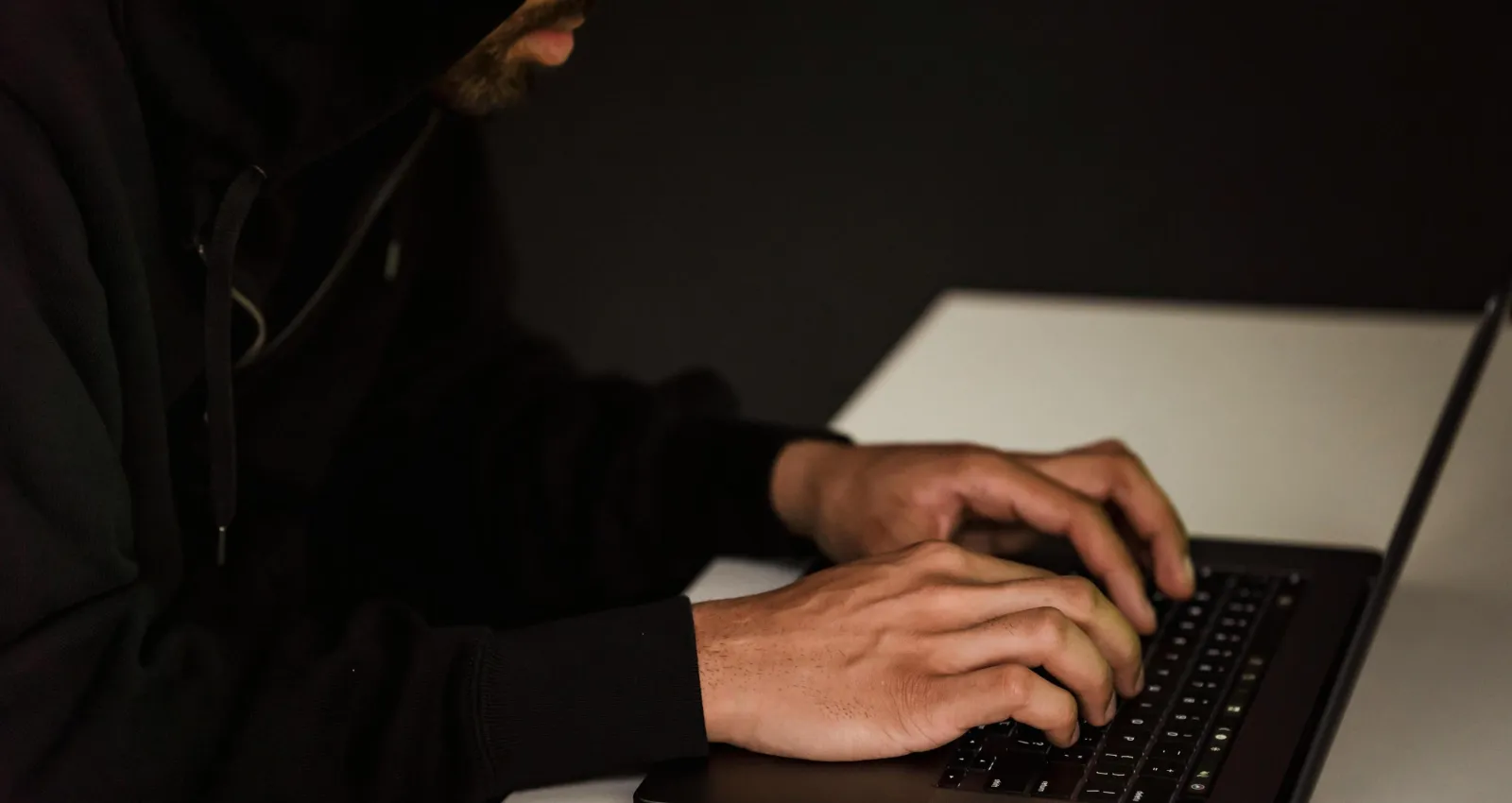 un hombre con capucha negra escribiendo en su laptop