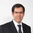 Hombre con traje y gafas cuadradas sonriendo a la cámara 