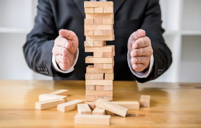 Persona tratando de que una torre hecha con bloques de madera no se caiga