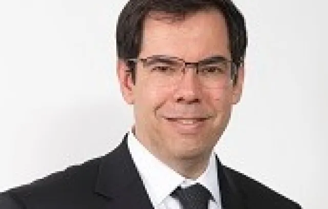 Hombre con traje y gafas cuadradas sonriendo a la cámara 