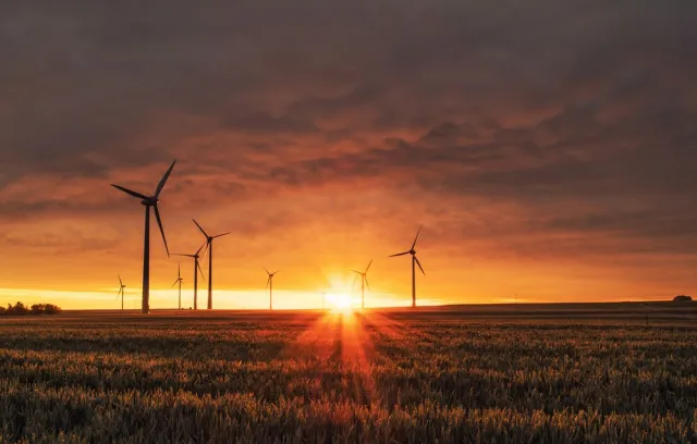Día de la energia, foto de una puesta de sol con una imagen de energia eólica de fondo