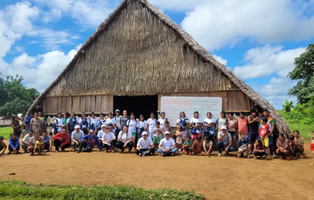 Foto de una casa en paja con 30 personas al frente de ella posando para una fotografía