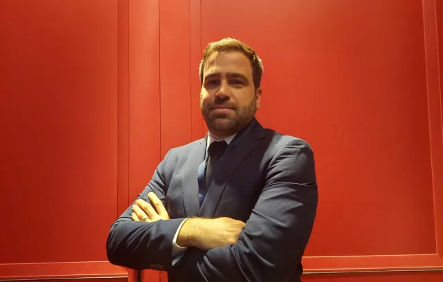 Hombre blanco y con barba cruzando sus brazos y mirando hacía la cámara