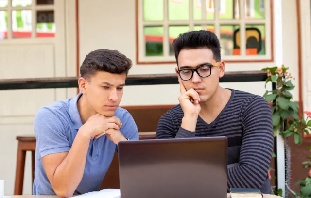 Foto de dos jóvenes mirando el computador mientras piensan