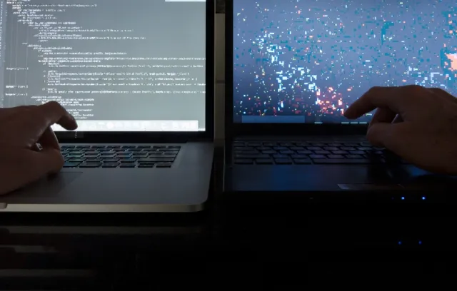 Foto de dos manos escribiendo sobre dos computadores portátiles